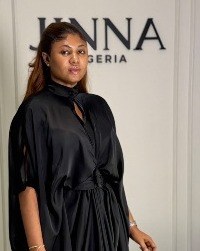 Woman in a black tie-neck dress beside the JINNA sign