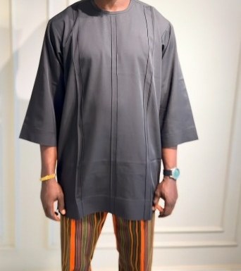 Man in a charcoal tunic with pintuck seams and striped trousers