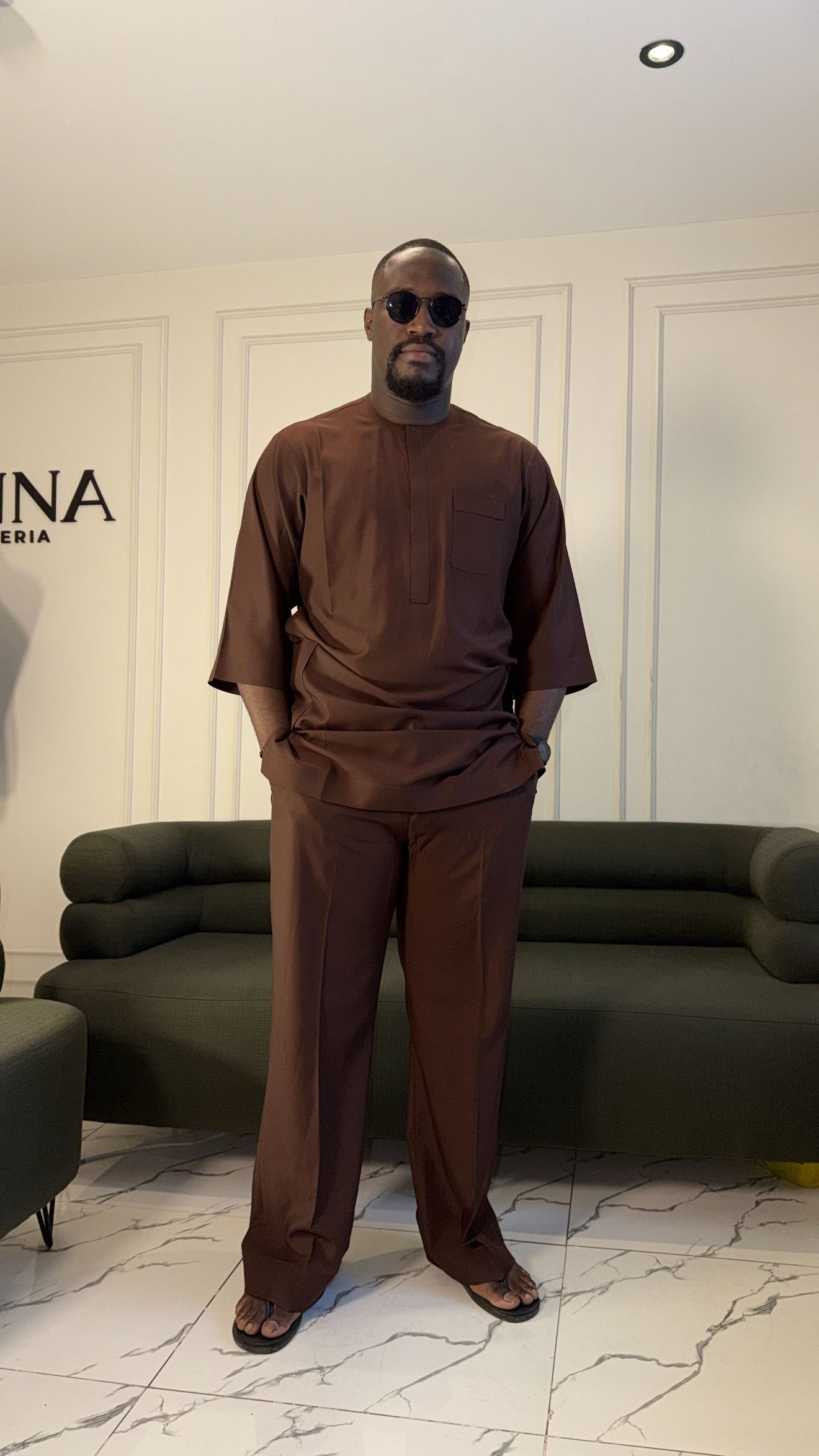 Man in a chocolate brown tunic and matching trousers standing in the JINNA showroom