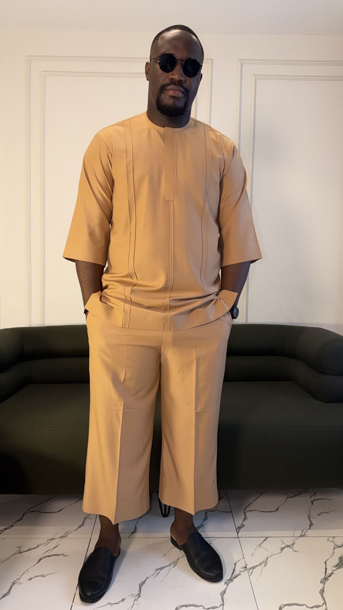 Man in a camel short-sleeve top and cropped wide trousers, hands in pockets